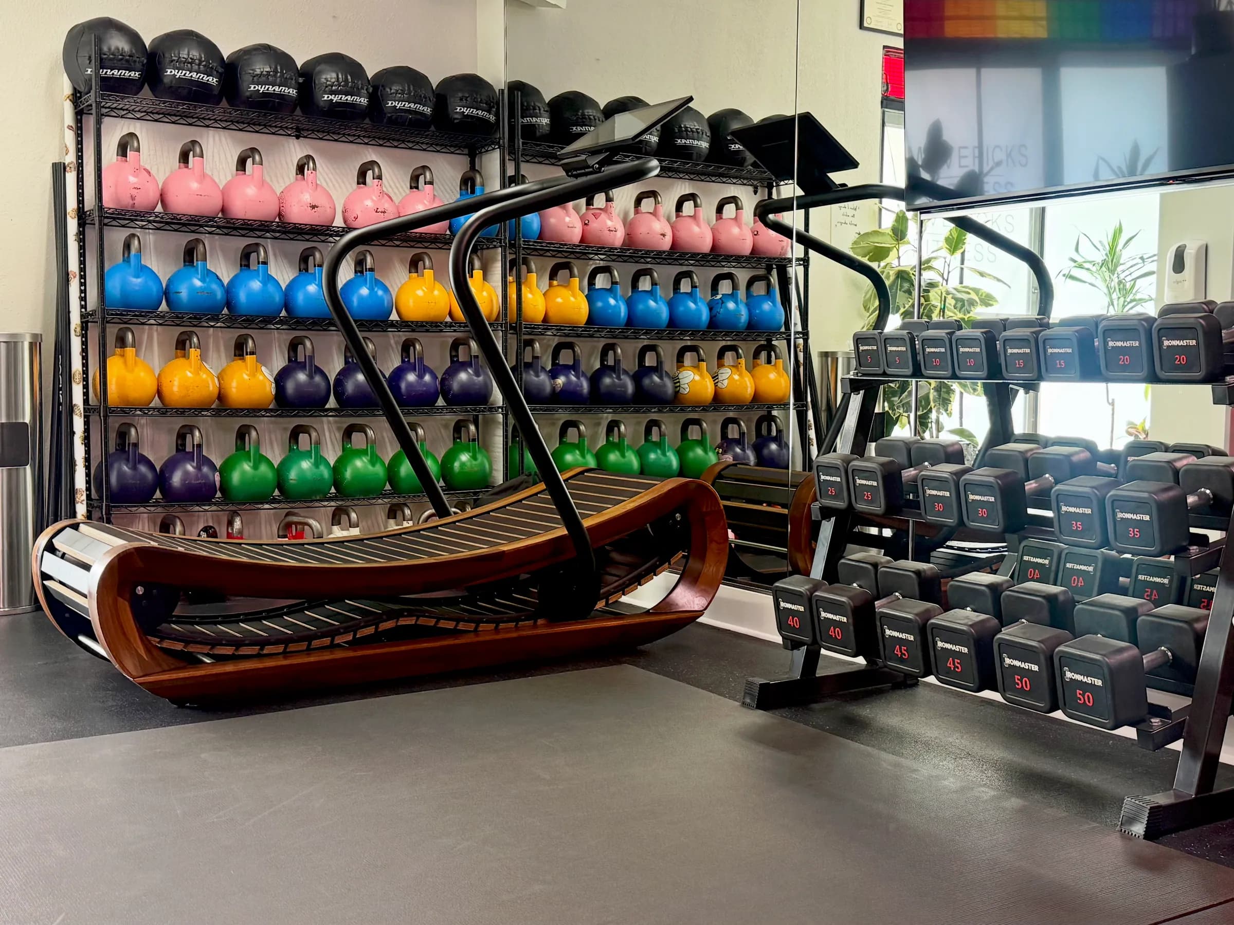 Dumbbell rack, curved treadmill, and the kettlebell and medicine ball wall at Mavericks Fitness